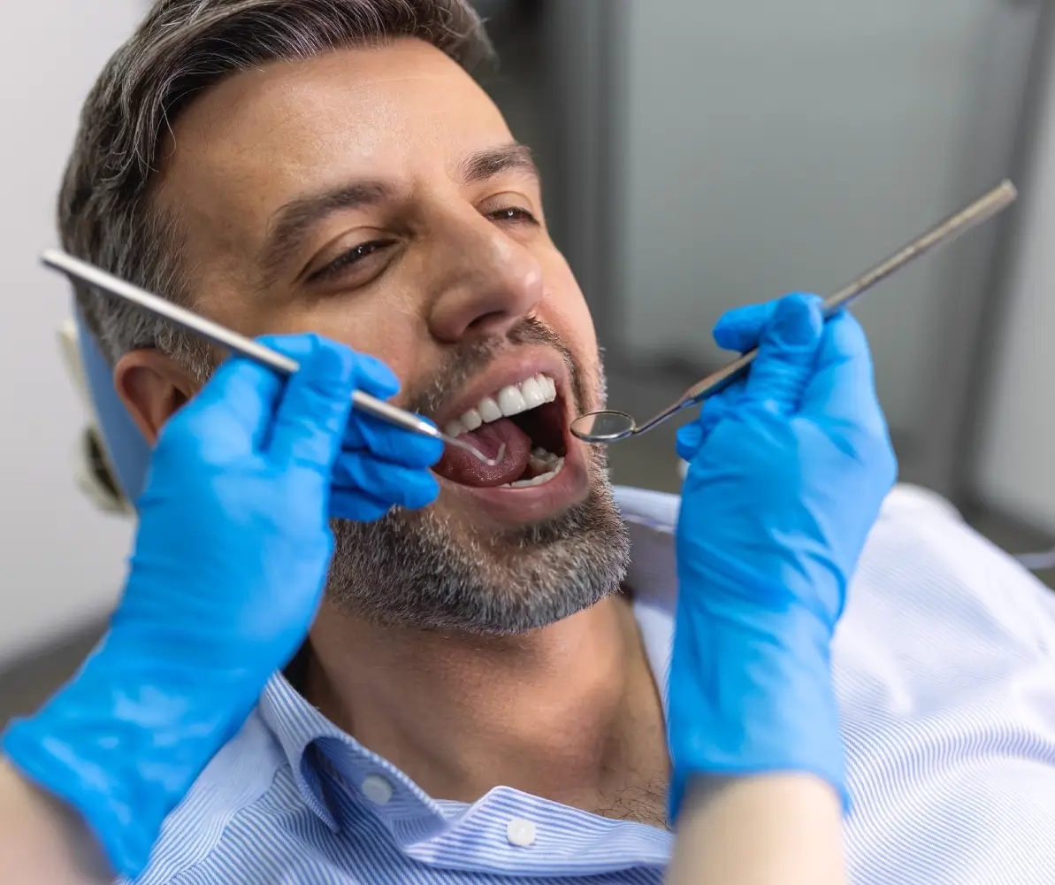 Man receiving dental check-up with tools.
