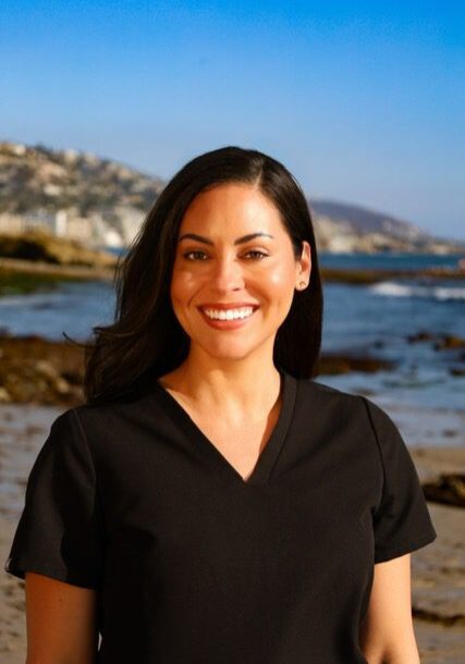 Smiling woman in black scrubs at the beach.