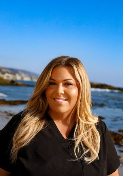 Smiling woman with long blonde hair by the ocean on a sunny day.